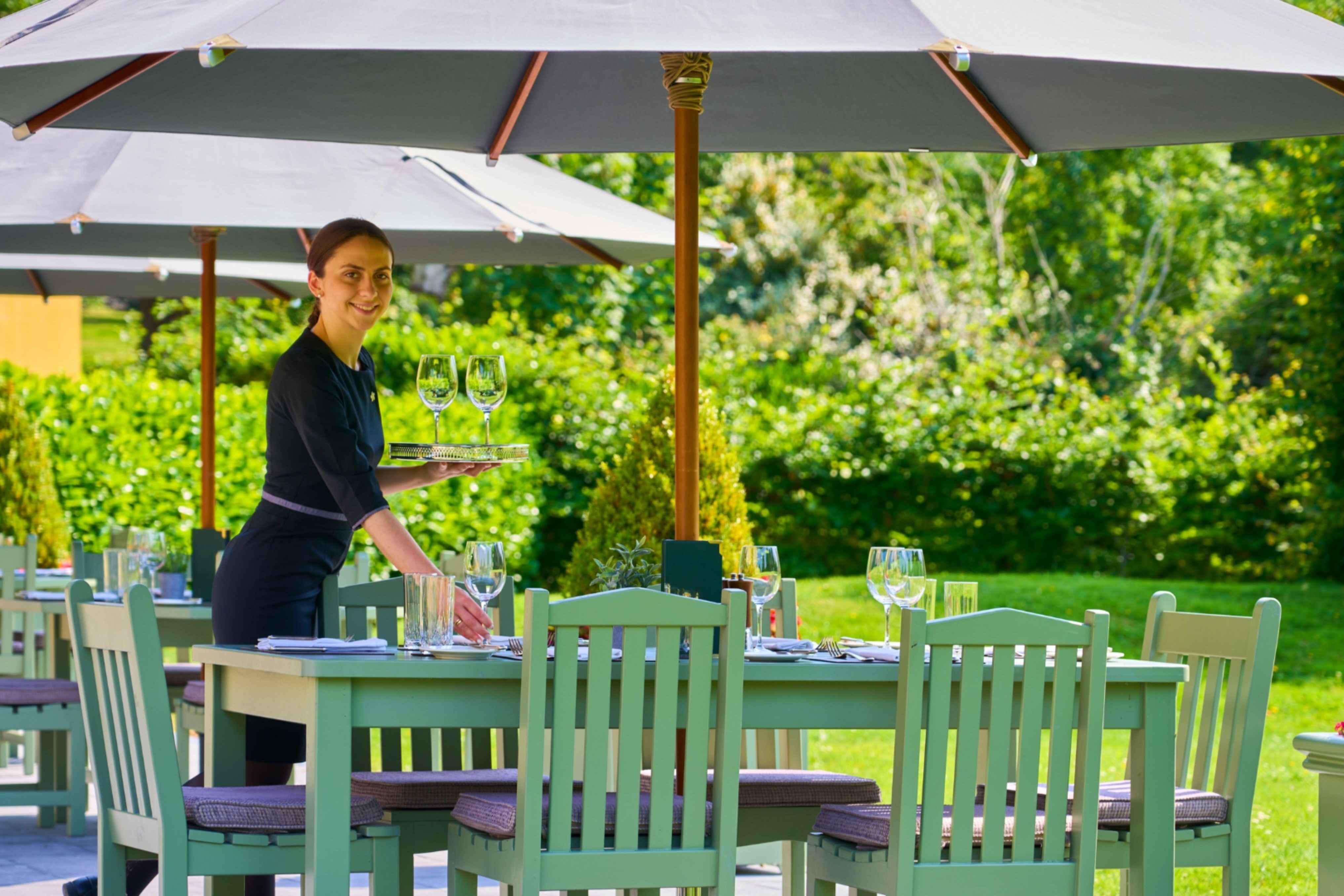 Charming Garden Terrace with Outdoor tables and a server offering attentive service amid blooming plants.