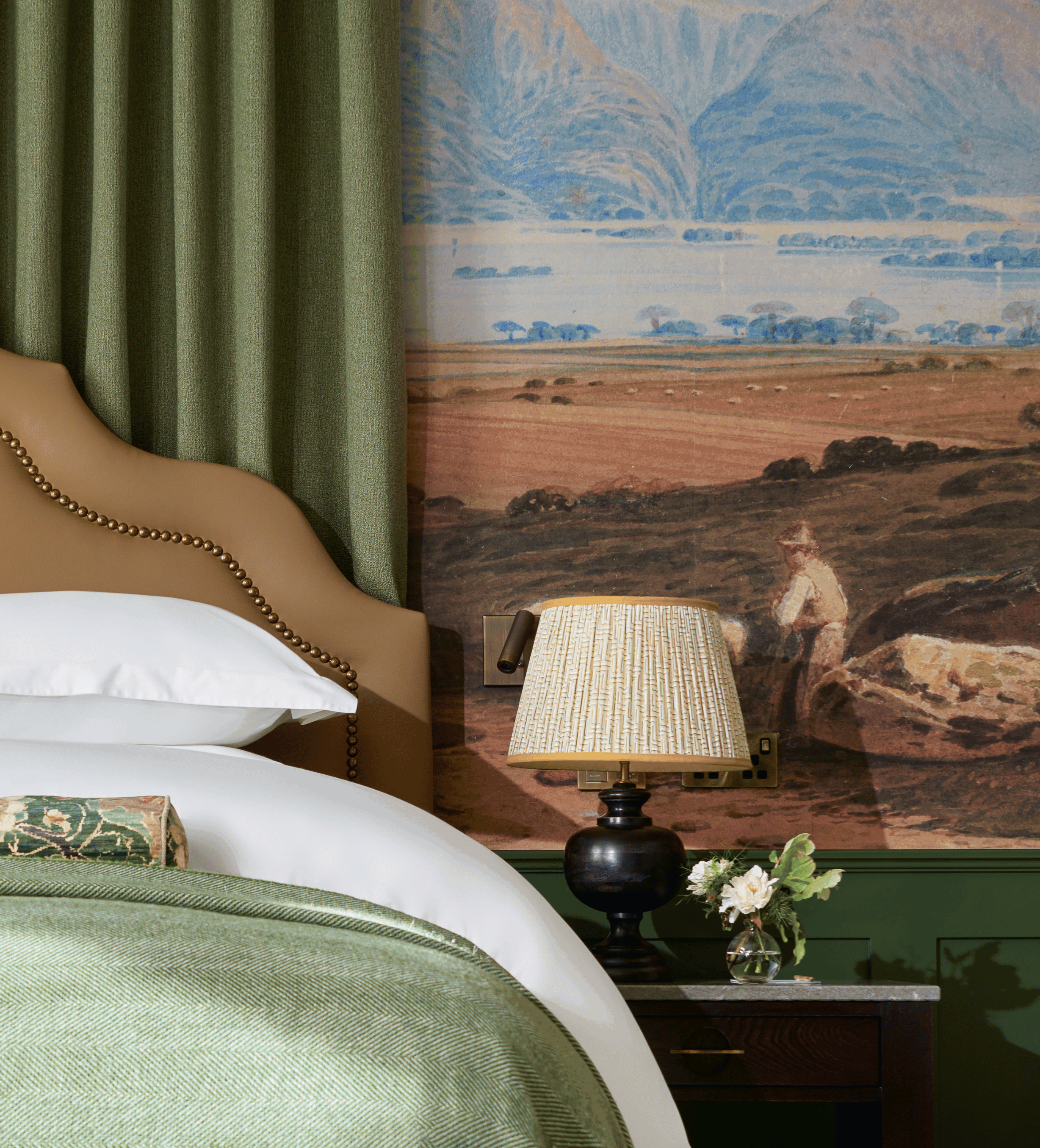 Bedside area has a polished rustic wooden table with a lamp on top and fresh flowers in a glass vase.