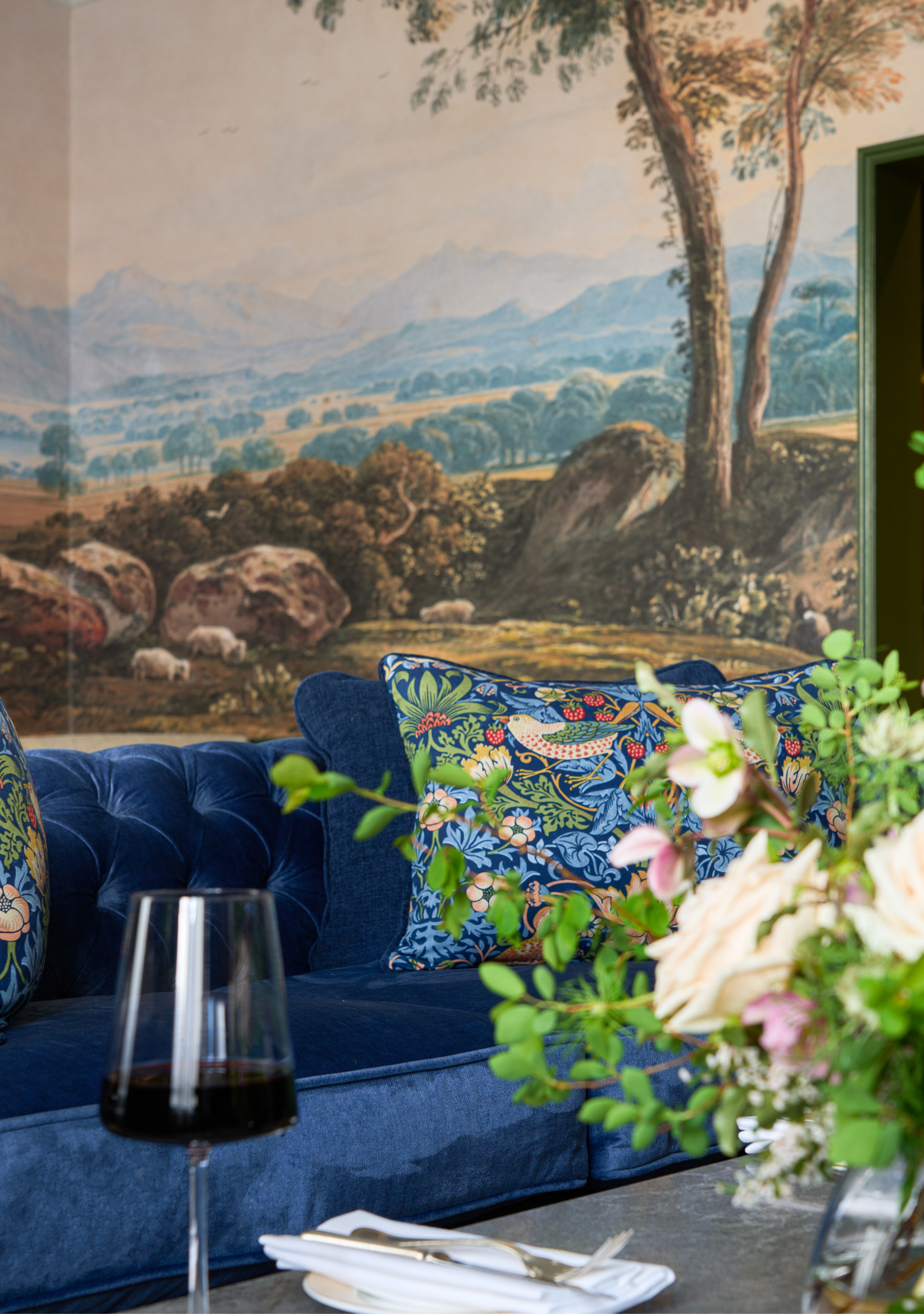 This is The Signature Suite's living room area. There is a beautiful royal blue couch and a glass of red wine of the guest.